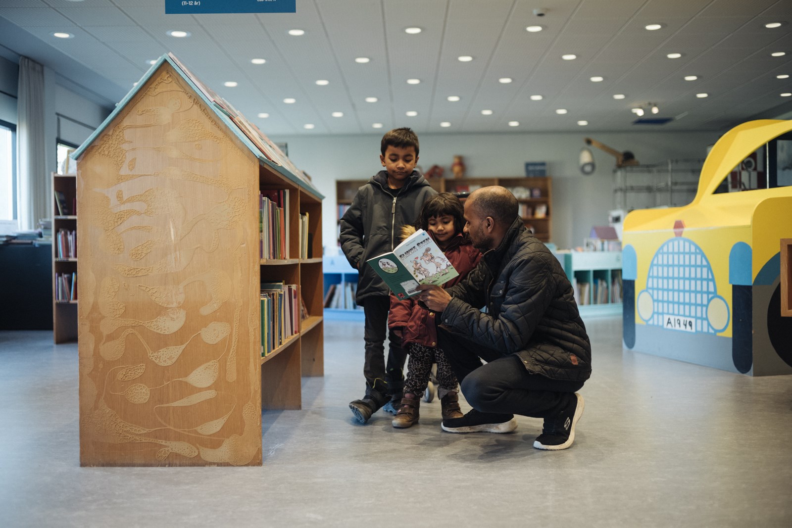 Far med to mindre børn kigger i en bog  på Vejle Bibliotek. Foto: Jonas Normann